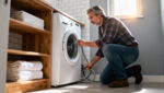 Homeowner Inspecting Washing Machine Supply Hoses Behind A Washer, Checking For Cracks And Bulges Near Shut-Off Valves