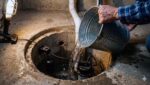 Homeowner Pouring Water From A Five-Gallon Bucket Into A Basement Sump Pump Pit To Test The Float Switch.