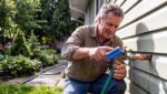 Homeowner Scrubbing An Outdoor Brass Hose Bib Connection On A Green-Sided South Surrey Home During Diy Spring Plumbing Maintenance