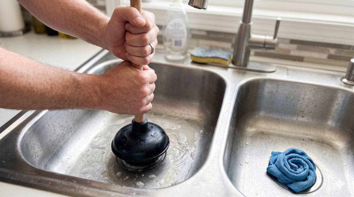 Homeowner Pouring Hot Water From A Kettle Into A Stainless Steel Kitchen Sink To Clear A Clog