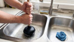 Unclog Your Kitchen Sink Without Chemicals Homeowner Pouring Hot Water From A Kettle Into A Stainless Steel Kitchen Sink To Clear A Clog