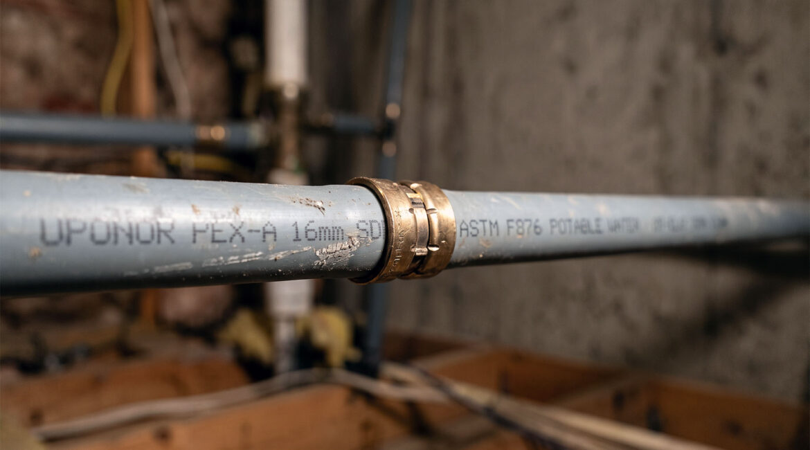 Poly B Pipe In A Bc Home, Grey Flexible Supply Line Joined By A Metal Crimp Ring Under Work Light