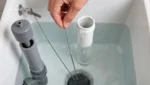 Running Toilet: Diy Fix Or Call A Plumber? Hand Holding The Flush Chain Inside A Toilet Tank, Checking The Seated Flapper Beside The Fill Valve And Overflow Tube.